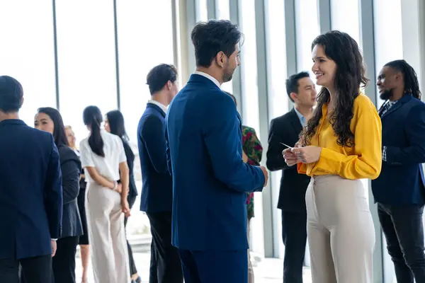 Businessman discussing with female leader about financial project intentionally while standing rounded with business people exchanging financial experience. Side view. Office hallway. Intellectual.