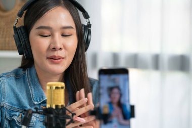 Asyalı sunucu canlı yayında canlı yayında canlı yayında sosyal medyada kulaklık takarak konuşuyor. Dinleyicileri modern stüdyoda koçluk yaparak selamlıyor. Taktik.