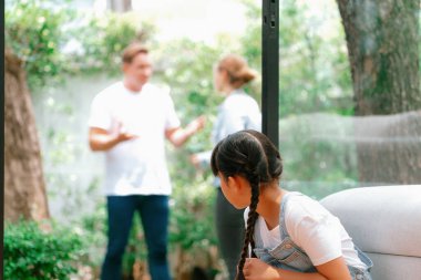 Stresli ve mutsuz genç kız arka planda ebeveynleri tartışırken köşede ağlayıp üzülüyor. Evde aile içi şiddet ve travmatik çocukluk depresyona dönüşür. Eşzamanlama
