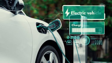 EV şarj kablosuna elektrik kablosu takılı. Çevre yeşil parkı ve yeşillik arka planında akıllı dijital batarya durum hologramını gösteriyor. Enerji sürdürülebilirliği teknolojik gelişim.