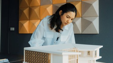 Ev modeli uzunluğunu ölçen Asyalı kadın mimar mühendisinin yakın çekimi. Genç, güzel proje yöneticisi ev modeli üzerinde çalışırken ev inşaatını kontrol ediyor. Yaratıcı tasarım konsepti. Yönlendirici.