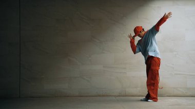 Yakışıklı koreograf gri arka planda sokak dansı yapıyor. Genç çekici erkek dansçı şık kıyafetler giyerken gösteri yapıyor. Hareketli bir adım. Uzayı kopyala Açık hava sporu 2024. Yumuşak bir şekilde..