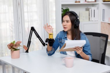 Sosyal medyada kulaklıkla canlı yayın yapan Asyalı sunucu modern stüdyoda yaşam koçluğu veya pazarlama dinleyicilerini selamlıyor. Taktik.