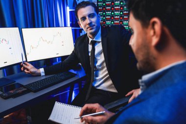 İki borsa simsarı dinamik yatırım grafiğini tartışıyor, yüksek kar eğilimli döviz borsası. İş yerindeki neon ışıkta finansal fayda verileri monitörde gösteriliyor. Satılabilir.