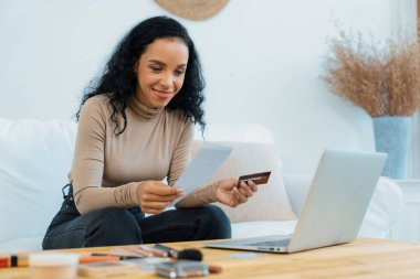 Genç mutlu bir kadın internetten alışveriş yaparak ürün satın alırken aynı zamanda internet üzerinden online kredi kartı ödeme sistemi ile çevrimiçi mağaza platformundan önemli siber güvenlik tarafından korunan ürünler sipariş ediyor.