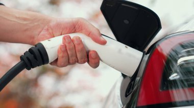 Temiz ve sürdürülebilir enerji kullanarak şarj istasyonundan şarj olmak için EV şarj cihazını EV vagonuna takın. Doğal koruma ve çevre dostu araba yolculuğu konsepti. Yükselt