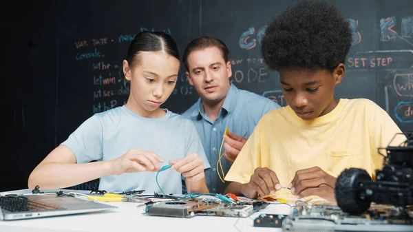 Smart mentor teach main board construction while diverse teenager learning system. Teacher explain about motherboard structure while academic student learning to use electronic equipment. Edification.