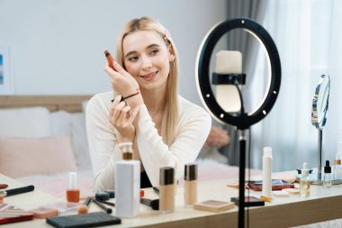 Sosyal medya için güzellik ve kozmetik video içeriği hazırlayan genç bir kadın. Seyirciye veya takipçiye nasıl sıvı ruj sürüleceğini gösterirken kamera ve ışık halkası kullanan bir güzellik blogcusu. Blithe