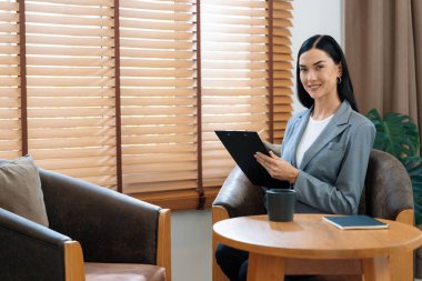 Psikiyatri ofisinde ya da terapi odasında koltukta oturan mutlu ve gülümseyen kadın psikolog portresi. Arkadaş canlısı ve profesyonel ruh sağlığı danışmanı ve terapisti. Blithe