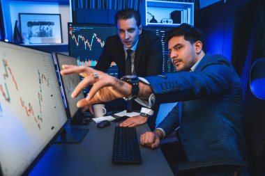 Borsa simsarları gece ekran ekranında yüksek kar grafiği yatırımına bakıyorlar. İş ortakları iş yerinde neon ışığı altında ticaret teknolojisi büyümesini tartışıyor. Satılabilir.