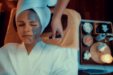 Kaplıca salonunun sakin atmosferi, üst düzey kadın müşteri sıcak mum ışığında kömür kömürü yüz kremi masajıyla kendini yenilemeye çalışıyor. Yüz bakımı ve güzellik konsepti. Sessiz.