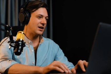 Sunucu kanalı akıllı yayıncı laptopta canlı sosyal medya uygulaması arıyor, kulaklık takıyor ve modern ofis stüdyosundaki mikrofonu kullanıyor. Bireysel.