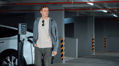 Genç adam EV elektrikli arabasıyla alışveriş merkezinin otoparkına gidiyor şehir merkezindeki şarj oluyor yeşil, temiz, yeniden şarj edilebilir elektrikli araç iç organları ile kentsel sürdürülebilirlik yaşam tarzını gösteriyor