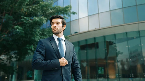 Handsome caucasian business man standing in front of building. Skilled investor looking around while pose cool at camera. Smart project manager wearing formal suit. Vision and professional. Exultant.