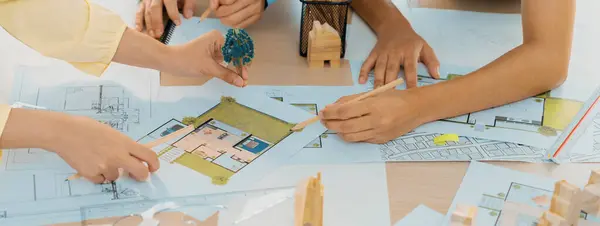 Professional architect engineer team discussion about architectural project on meeting table with wooden block and blueprint scatter around. Design and cooperate concept. Closeup. Delineation.