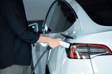 Genç adam EV elektrikli arabasıyla alışveriş merkezinin otoparkına gidiyor şehir merkezindeki şarj oluyor yeşil, temiz, yeniden şarj edilebilir elektrikli araç iç organları ile kentsel sürdürülebilirlik yaşam tarzını gösteriyor