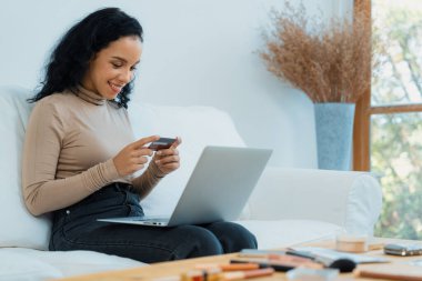 Genç mutlu bir kadın internetten alışveriş yaparak ürün satın alırken aynı zamanda internet üzerinden online kredi kartı ödeme sistemi ile çevrimiçi mağaza platformundan önemli siber güvenlik tarafından korunan ürünler sipariş ediyor.