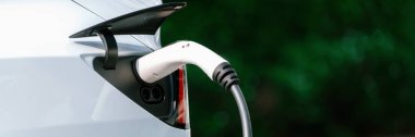 Elektrikli araç portuna bağlı EV şarj prizi kolu şarj istasyonundan şarj oluyor. Modern tasarlanmış EV araba ve daha iyi bir gelecek için temiz enerji sürdürülebilirliği. Panorama Senkronları