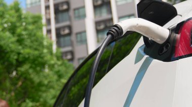Yazın yeşil sürdürülebilir şehir bahçesinde elektrikli araba şarj oluyor. Kentsel sürdürülebilirlik yaşam tarzı yeşil temiz yeniden şarj edilebilir enerji elektrikli BEV araç iç organları