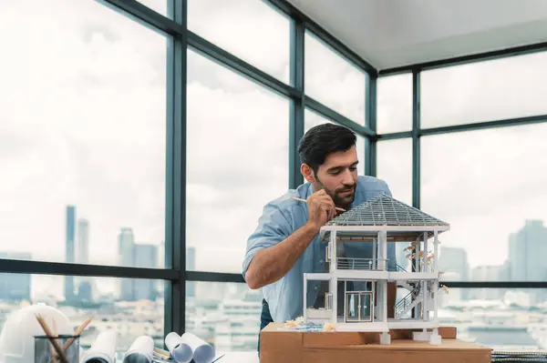 Professional caucasian architect engineer inspect modern house model with skyscraper view while comparing between house model and blueprint with project plan and architectural equipment. Tracery.