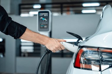 Genç adam EV elektrikli arabasıyla alışveriş merkezinin otoparkına gidiyor şehir merkezindeki şarj oluyor yeşil, temiz, yeniden şarj edilebilir elektrikli araç iç organları ile kentsel sürdürülebilirlik yaşam tarzını gösteriyor