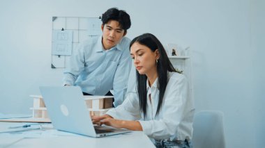 Profesyonel Asyalı erkek mimar ev modelinin uzunluğunu ölçmek için cetvel kullanırken, beyaz tenli genç meslektaşı ev modeliyle toplantı masasındaki verileri analiz etmek için dizüstü bilgisayar kullanıyor. Tertemiz..