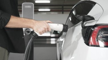 Genç adam EV elektrikli arabasıyla şehir merkezindeki alışveriş merkezinin otoparkına gidiyor şehir merkezindeki sürdürülebilirlik yaşam tarzını yeşil, temiz, yeniden şarj edilebilir elektrikli araç iç organlarıyla şarj ediyor.