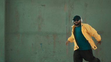 Hippi sokak, şehir merkezinde ayak izleri gösteriyor ya da pratik yapıyor. Hareketli genç break dansçı hareketi ve kol ve bacak esneme hareketi. Açık hava sporu 2024. Gri arka plan. Hip hop modası. ÇalışmaComment.