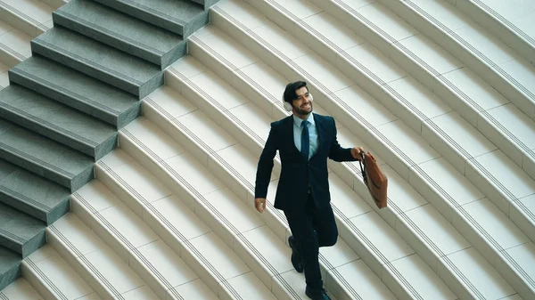 Happy business man listening to music from headphone while walking down at stairs. Executive manager dancing to celebrate increasing sales or successful project or getting new position. Exultant.