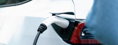 Panorama kapatma EV şarj kolu fişe takıldı veya elektrikli arabaya bağlandı, temiz çevre için sıfır CO2 emisyonu ile alternatif ve sürdürülebilir enerjiyle EV araba aküsünü şarj etti. Kalıcı