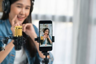 Asyalı sunucu canlı yayında canlı yayında canlı yayında sosyal medyada kulaklık takarak konuşuyor. Dinleyicileri modern stüdyoda koçluk yaparak selamlıyor. Taktik.