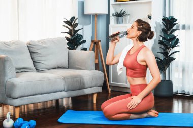 Sportif ve atletik kadınlar spor paspası üzerinde su içiyorlar. Vücut egzersizlerini bitirdikten sonra evde sağlıklı fiziğe ve spor yaşam tarzına uygun bir yaşam sürüyorlar. Gaiety evde egzersiz eğitimi.