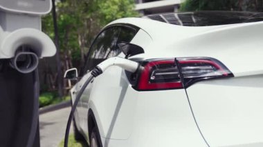 Yavaş çekim EV elektrikli araba yazın yeşil sürdürülebilir şehir bahçesinde şarj oluyor. Kentsel sürdürülebilirlik yaşam tarzı yeşil temiz yeniden şarj edilebilir enerji elektrikli BEV araç iç organları