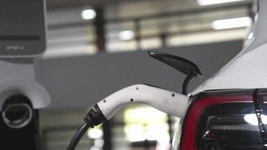 Şehir merkezindeki kapalı otoparkta yavaş çekimde EV elektrikli araba şarj oluyor. Şehir merkezinde sürdürülebilirlik yeşili, yeniden şarj edilebilir elektrikli araç iç organları.