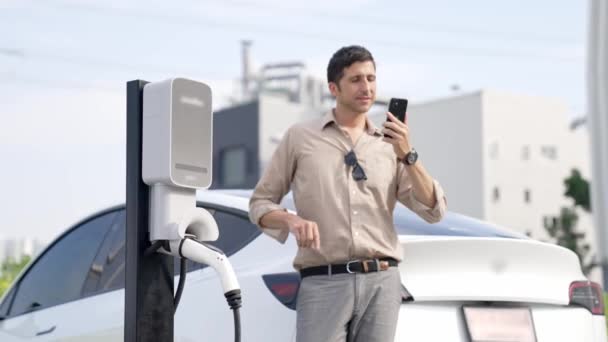 慢动作男子使用智能手机支付电费的公共电动车收费站在城市商业购物中心停车场 利用越野车的现代环境和可持续城市生活方式 — 图库视频影像