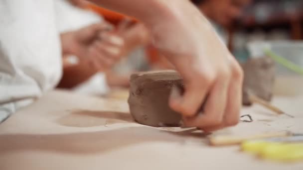 粘土の彫刻ツールスカルプカップを使用した高校生の手のクローズアップ 陶芸のワークショップで粘土のピースを遊んだりモデリングしたりしながら活動している多様な子供たち バックグラウンド イスラーム主義 — ストック動画