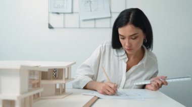 Modern ofisteki ev modelini planla ölçmek için kalem işaretleme noktası ve cetvel kullanmaya odaklanan genç ve güzel mimar mühendisinin yakın çekimi. Yaratıcı tasarım ve mimar konsepti. Tertemiz..