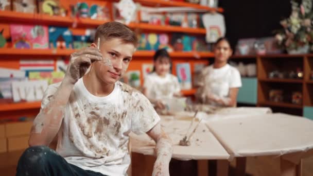 在艺术课上 学生们一边看一边把画笔放在耳朵后面 看起来很开心 不同的学生一起上陶器课 高中生穿着沾满泥巴的白衬衫时 微笑着 — 图库视频影像