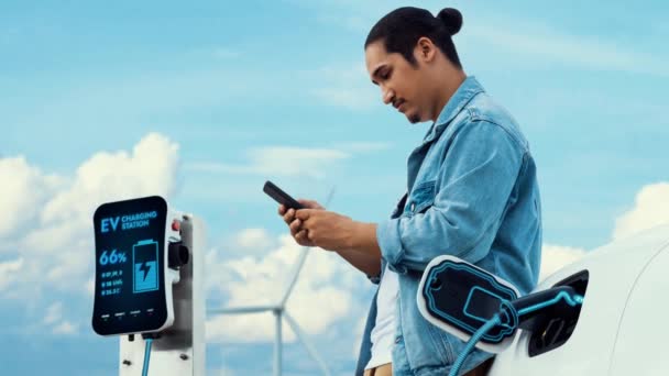 Pria Asia Menggunakan Smartphone Sementara Mobil Listrik Mengisi Energi Dari — Stok Video