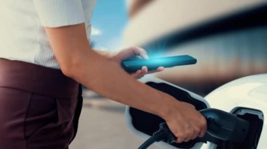 Modern bir kadın EV şarj cihazını EV 'nin şarj edildiği istasyondan şarj edilen arabasını şarj etmek için elektrikli otomobil portuna yerleştirir. Yenilikçi alternatif sürdürülebilir enerji kullanımı. İnceleyin
