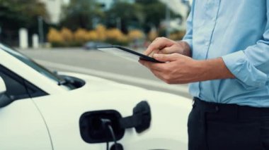 Modern iş adamı akıllı telefonun 3D hologramından batarya durumunu kontrol ederken EV arabasının şarj olan enerjisini kontrol ediyor. Gelecekteki EV otomotiv teknolojisinin yenilikçi teknolojik gelişimi. İnceleyin