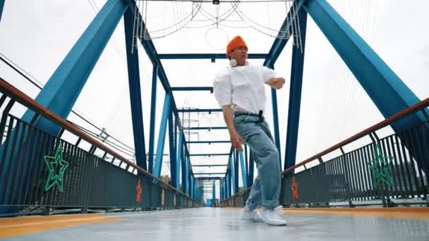 プロのブレイクダンサーが橋でストリートダンスの足跡を行います アジアのヒップスターは フリーズポーズをしている間 ヘッドフォンを着用します ブレイクダンサー ストリートダンサーフリースタイルのコンセプト アウトドアスポーツ 2024 スプライトリー — ストック動画