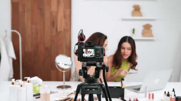 リアビュー一覧カメラ画面表示2人の女性インフルエンサーがライブストリーミングビデオレビューメイクアップソーシャルメディアやブログを撮影します マーケティングレコーディングのための化粧品の鮮やかなスタジオ照明を持つ少女 — ストック動画