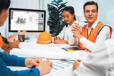 Mimari proje üzerinde birlikte çalışan çeşitli inşaat mühendisi ve müvekkil grupları, inşaat planını gözden geçirip toplantı masasında plan oluşturuyorlar. Tedbirli