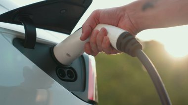 Otomobil yolculuğu sırasında elektrikli araba için şarj olan yakın çekim adamı. Ormanda ya da güneş ışığıyla birlikte ulusal parkta. Tatil ve tatil boyunca çevre dostu seyahat. Yükselt