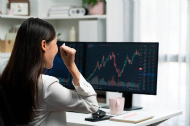 Başarılı genç Asyalı iş kadını, modern ofisteki bilgisayar ekranlarında dinamik iş grafiği üzerine borsada yumruklaşarak en yüksek karı elde ediyor, finansal teknolojiyi analiz ediyor. Taktik.