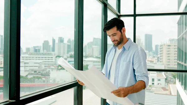 Professional architect engineer or male worker in casual outfit looking at skyscraper and city view while holding project plan. Creative design, civil engineering, building construction. Tracery