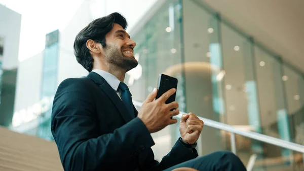 Successful business man celebrate successful project while sitting at stairs. Smart project manager getting new gob, getting promotion, increasing sales while calling friends by using phone. Exultant.