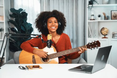 Genç Afrikalı Amerikalı müzisyenin sunucu kanalı gitar çalıyor, şarkı söylüyor, stüdyoda dizüstü bilgisayardan yayın yapıyor. Kulaklık dekorasyonu ve mikrofon kaydı. Tatlandırıcı.