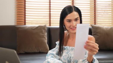 Mutlu bir kadın, faturalarını internet üzerinden öderken gülümseyerek kanepede oturur, tüm faturaları tek seferde ödemenin rahatlığını taktir eder ve kredi kartının sunduğu ödülün tadını çıkarır. Blithe